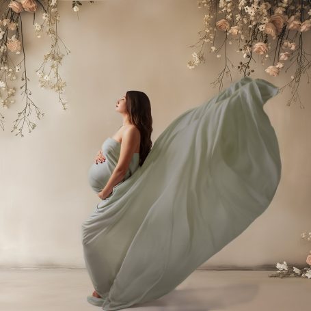 Schwangere Frau in fließendem grünen Kleid, umgeben von Blumen und sanftem Licht.