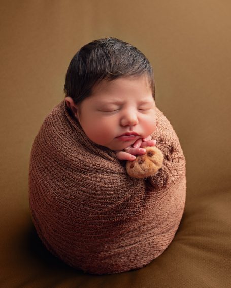 Schlafendes Neugeborenes in brauner Decke mit kleinen Händen und dunkelhaarig.