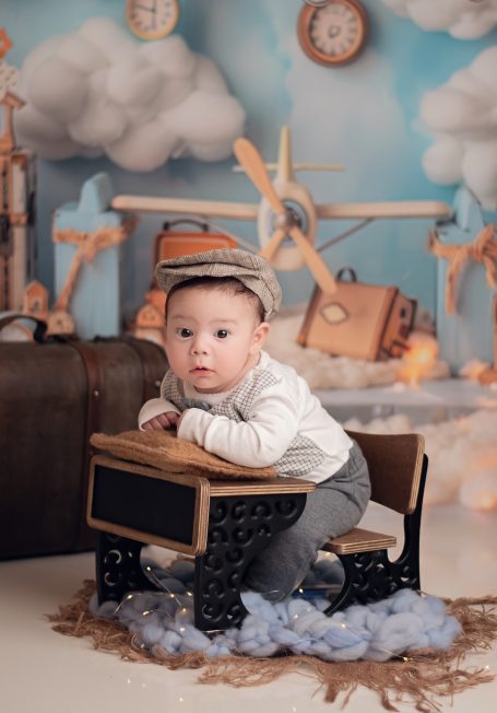 Ein kleiner Junge sitzt auf einem Tisch im Retro-Stil, umgeben von Spielzeug und Wolken.