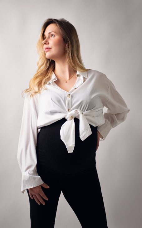 Schwangere Frau in weißem Hemd, das über ihrem Bauch geknotet ist, mit langem Haar.