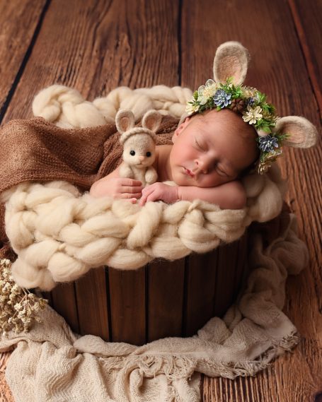 Schlafendes Baby mit Tierohren und Stofftier in einem Korb, umgeben von weicher Decke.