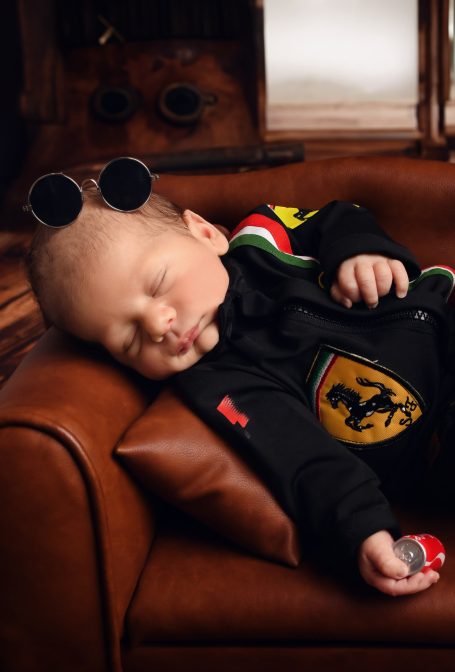 Schlafendes Baby mit Sonnenbrille, in schwarzem Outfit, auf einer Couch.