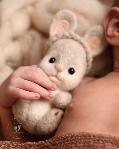 Ein Hand hält eine kleine, wollene Hasenfigur mit großen Augen und Ohren.