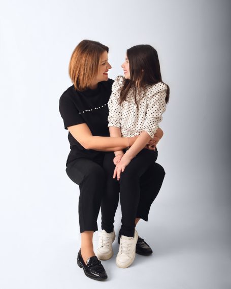 Eine Frau sitzt und umarmt ein Mädchen, beide lächeln einander an.