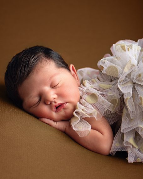 Schlafendes Baby in einem weißen Kleid mit Blumen auf einem braunen Hintergrund.