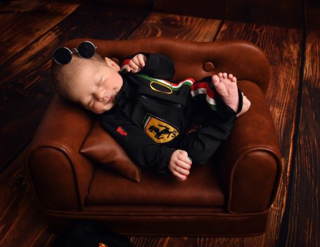 Ein schlafendes Baby in einem schwarzen Outfit auf einer kleinen braunen Couch.