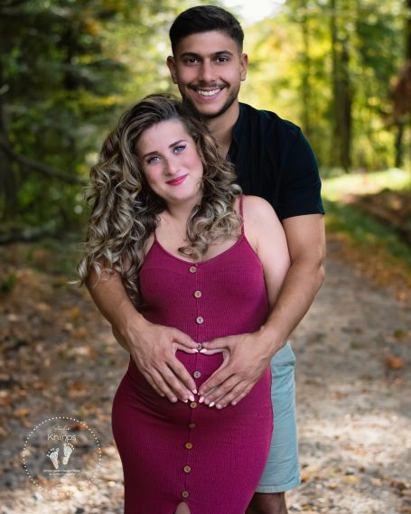 Paar in der Natur, die einen Babybauch liebevoll mit den Händen umarmt.