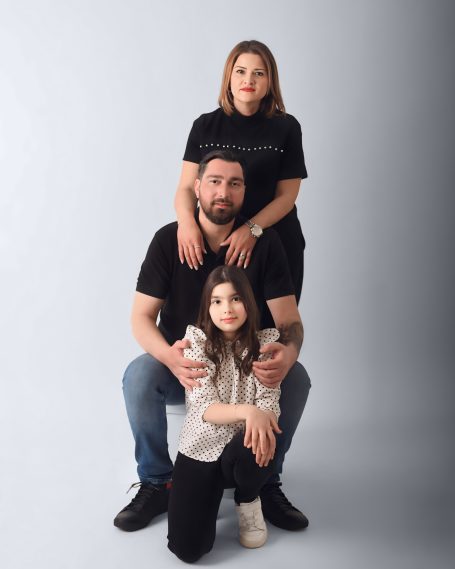 Familie posiert, der Vater sitzt, die Mutter steht hinter ihm, das Kind sitzt vorne.