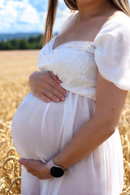 Schwangere Frau in einem weißen Kleid steht in einem goldenen Feld.