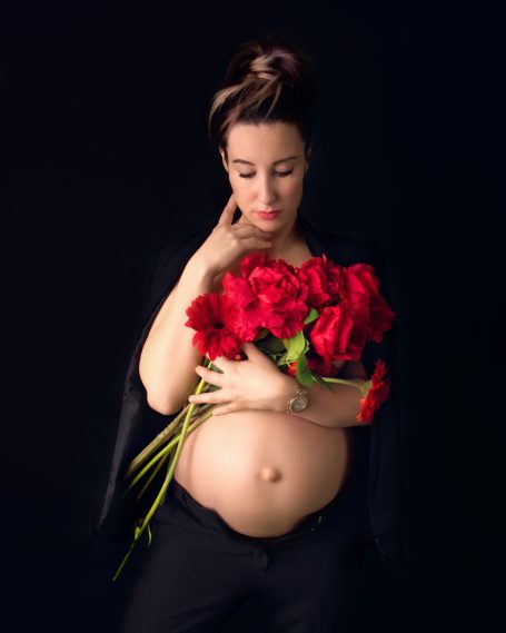 Schwangere Frau mit roten Rosen, nachdenklicher Gesichtsausdruck, schwarzer Hintergrund.