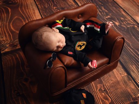 Ein schlafendes Baby in einem roten und schwarzen Outfit auf einem kleinen braunen Sofa.