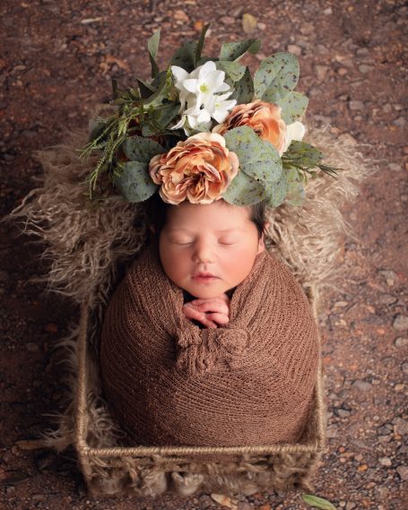 Neugeborenes Baby, in braunem Tuch gewickelt, mit Blumenkranz auf dem Kopf.