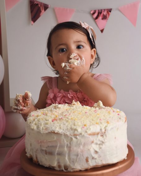 Kleines Mädchen mit rosa Kleid, das Kuchen mit beiden Händen isst.