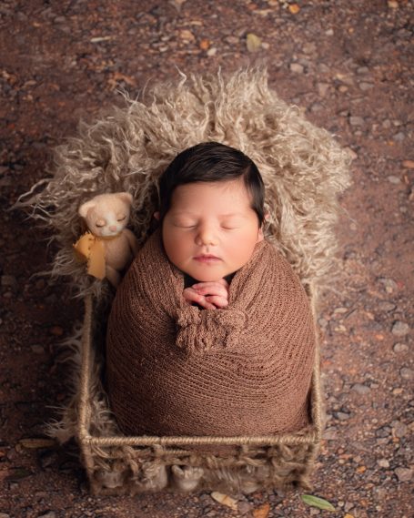 Neugeborenes Baby, in braunes Tuch gewickelt, in einem Korb auf weichem Untergrund.