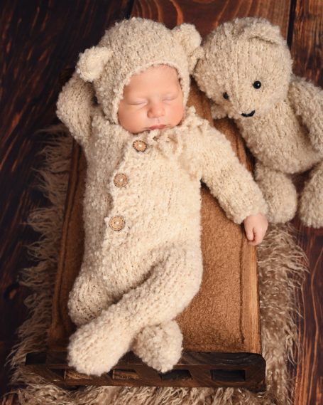 Ein schlafendes Baby in einem kuscheligen, hellen Bärenanzug neben einem Plüschbär.