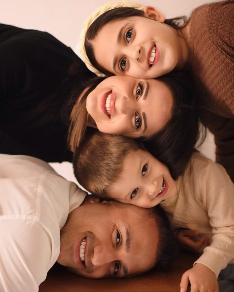 Eine glückliche Familie mit zwei Erwachsenen und zwei Kindern, eng umarmt und lächelnd.