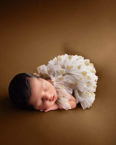 Schlafendes Baby in einem blumigen Kleid auf einem braunen Hintergrund.