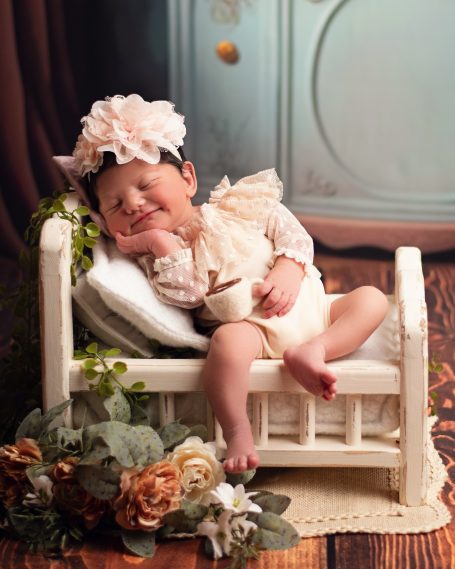 Ein schlafendes Baby in einem kleinen Bett mit Blumen und einer großen Haarschleife.