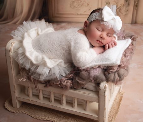 Neugeborenes Baby schläft auf einer kleinen Ruhebank, umgeben von weichem Material.