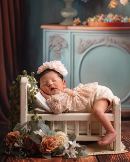 Schlägendes Baby in einem kleinen Bett, umgeben von Blumen und dekorativem Hintergrund.