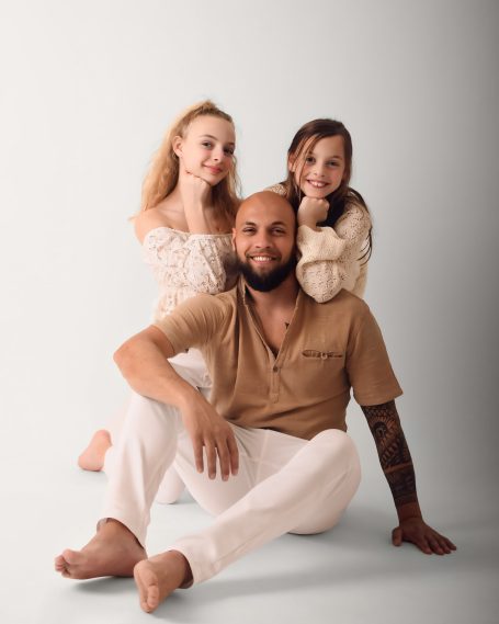 Ein Mann sitzt lächelnd mit zwei Kindern, die hinter ihm stehen und ebenfalls lächeln.