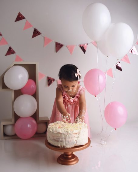 Kleines Mädchen in einem rosa Kleid mit einer Torte und Luftballons bei einer Feier.