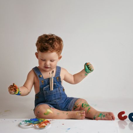 Ein neugieriges Kleinkind, das mit bunten Farben auf dem Boden spielt.
