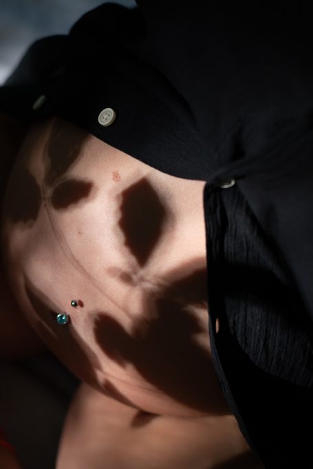 Abstrakte Schatten auf einem Bauch mit Piercing, in sanften Licht- und Dunkelheitstönen.
