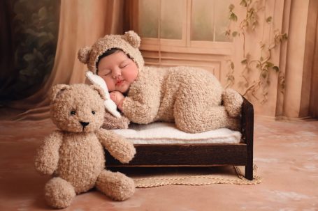 Schlafendes Baby in einem Bärenkostüm auf Bett, neben einem großen Plüschbären.