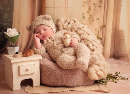 Ein schlafendes Baby in einem gemütlichen, beigen Overall, umgeben von Plüschtieren.