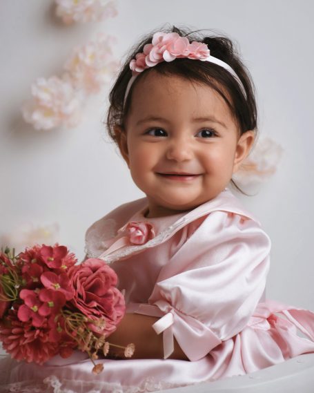 Ein lächelndes Kleinkind in einem rosa Kleid mit Blumenstrauß.
