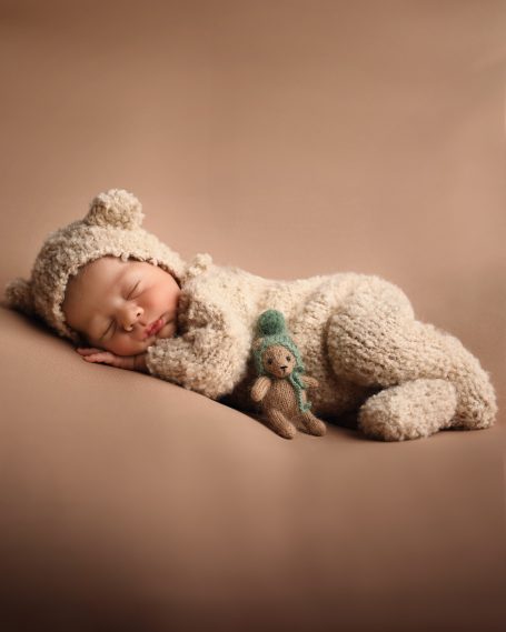 Ein schlafendes Baby in einem Bärenanzug hält ein kleines Stofftier.