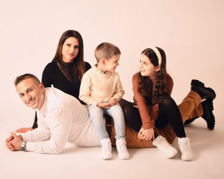 Eine Familie mit zwei Erwachsenen und zwei Kindern sitzt auf dem Boden und lächelt.