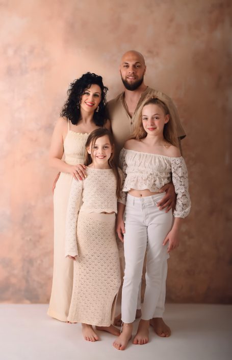 Familienfoto mit zwei Erwachsenen und zwei Mädchen in hellen, modischen Outfits.