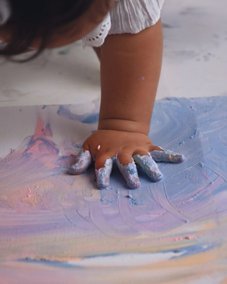 Ein Kind drückt seine Hand in farbige Malerei auf Papier.