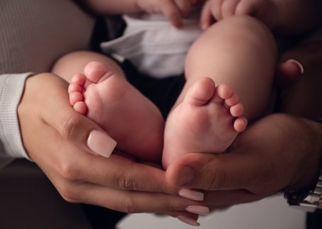 Hände halten die kleinen Füße eines Babys, die sanft und rosig sind.
