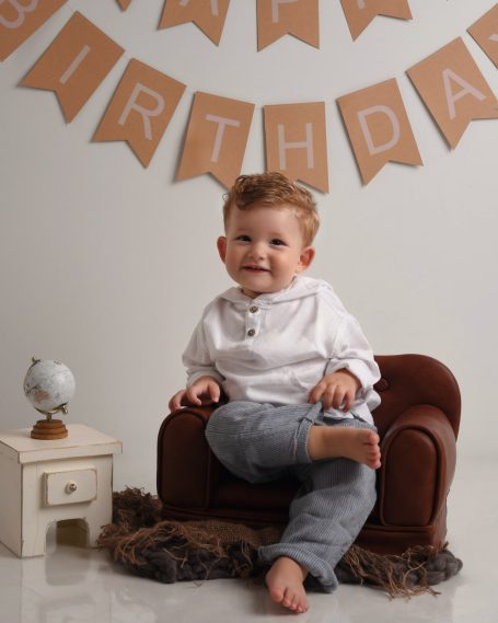 Ein lächelndes Kind sitzt auf einem kleinen Sessel vor einer Geburtstagsdekoration.