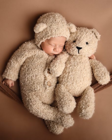 Ein schlafendes Baby in einem Bärenkostüm, umarmt ein ähnliches Kuscheltier.