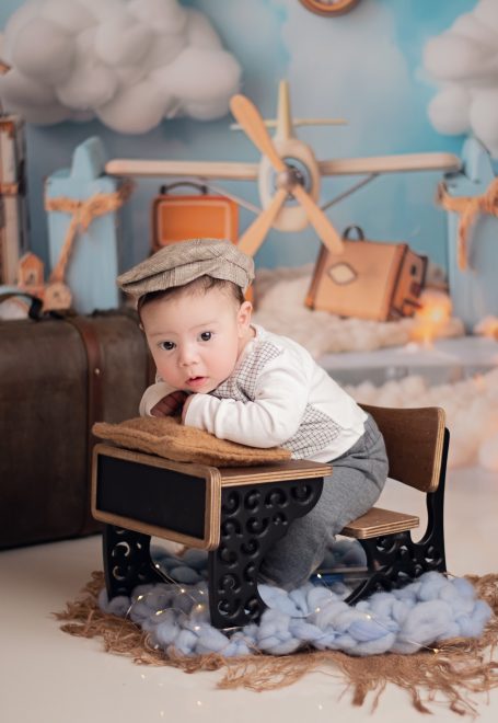 Ein kleiner Junge mit einer Mütze sitzt auf einem Holzstuhl in einer dekorativen Umgebung.