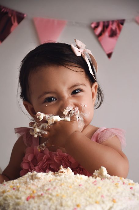 Ein kleines Mädchen in einem rosa Kleid isst Kuchen und spielt mit Sahne.