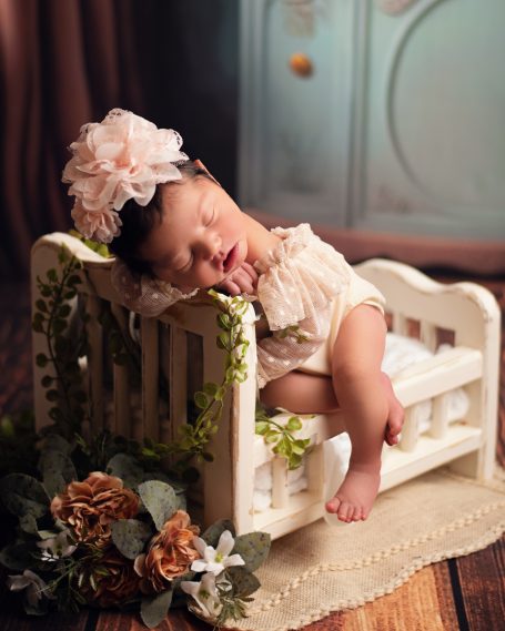 Schlafendes Baby in einem kleinen Bett mit Blumen und einer großen Haarschleife.