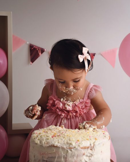 Ein kleines Mädchen in einem rosa Kleid, das eine Torte mit Freude erkundet.