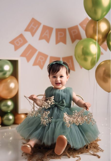 Ein kleines Mädchen in einem grünen Kleid mit goldenen Details sitzt umgeben von Dekorationen.