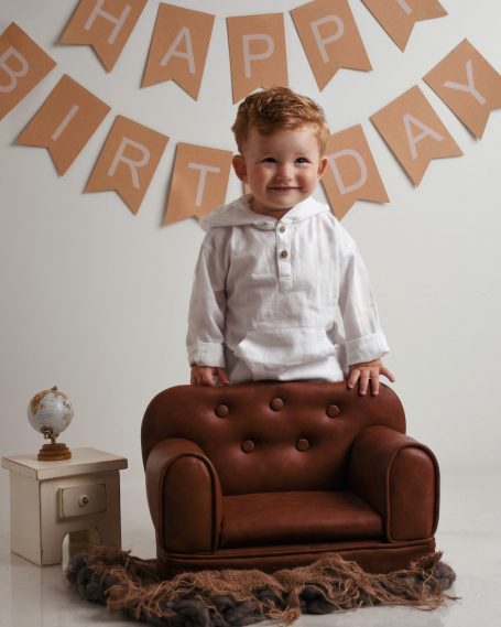 Ein lächelnder Junge steht auf einem kleinen braunen Sofa, umgeben von einem Geburtstagsbanner.